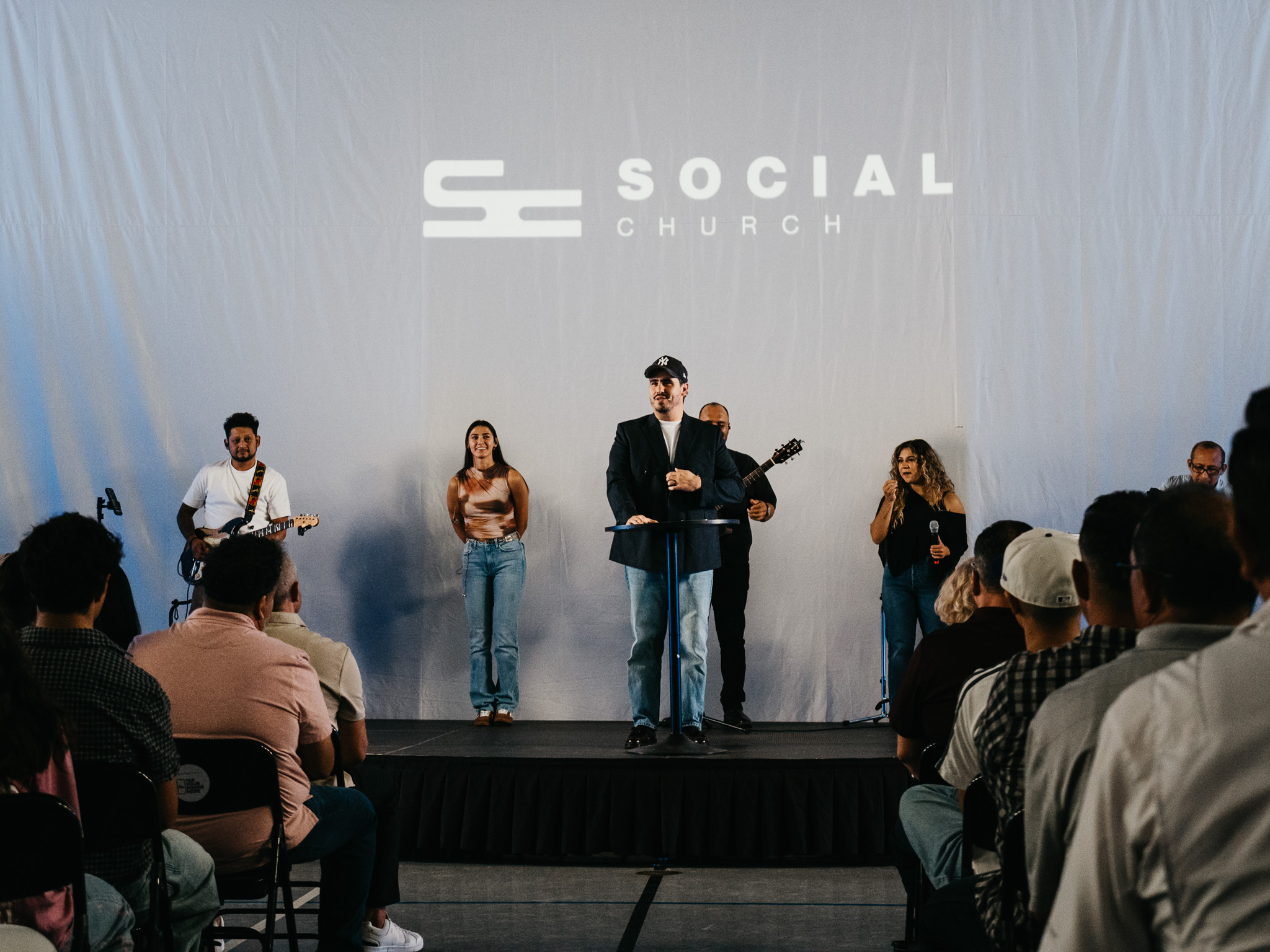 Social Church gathered for worship with the speaker and worship team on stage
