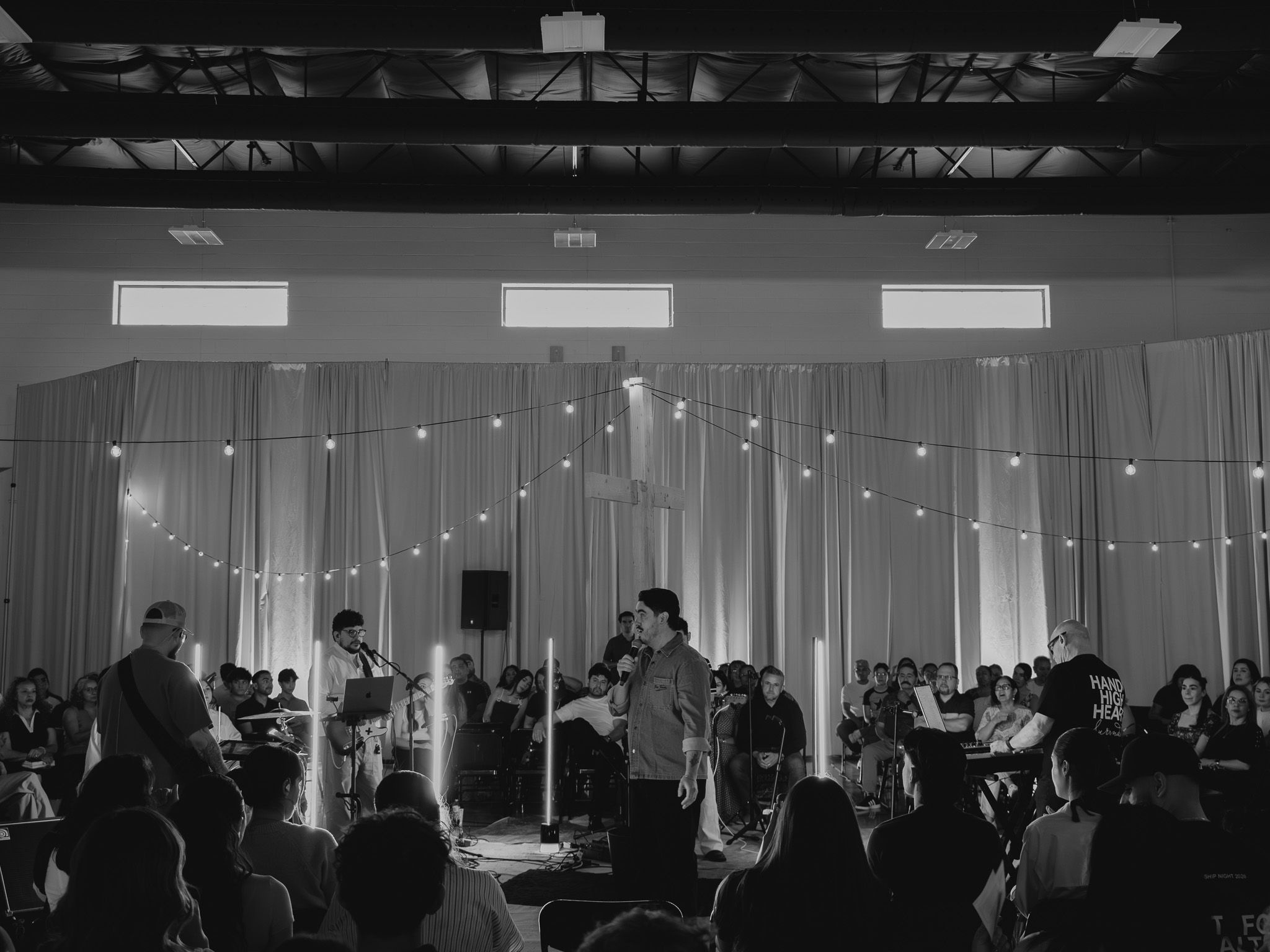 Social Church gathered for worship beneath string lights and a wooden cross.